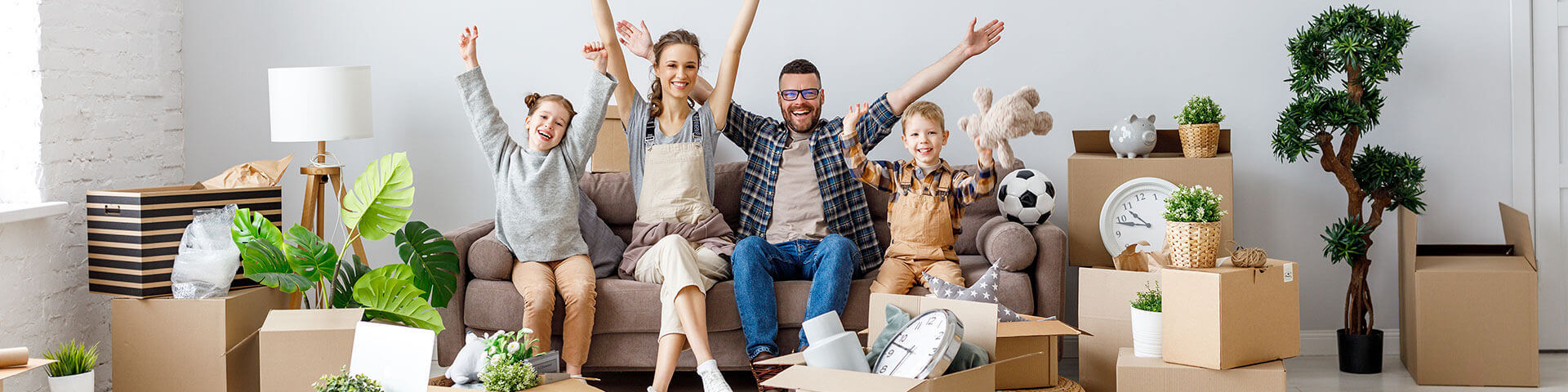 glückliche Familie sitzt auf Sofa mit Umzugskartons im Raum verteilt