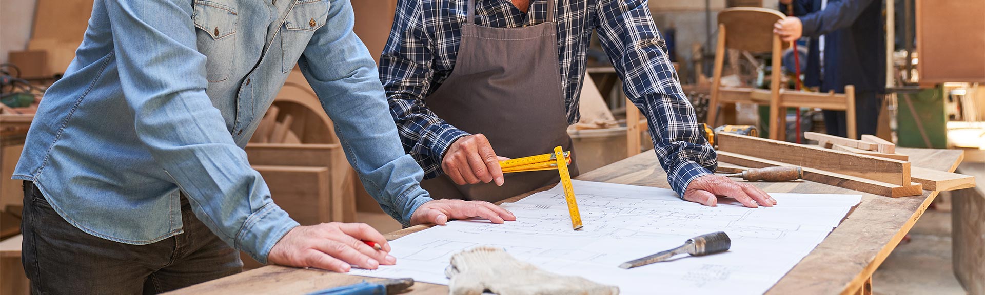 Handwerker und Tischlerauszubildender diskutieren über einen Bauprojekt-Entwurf
