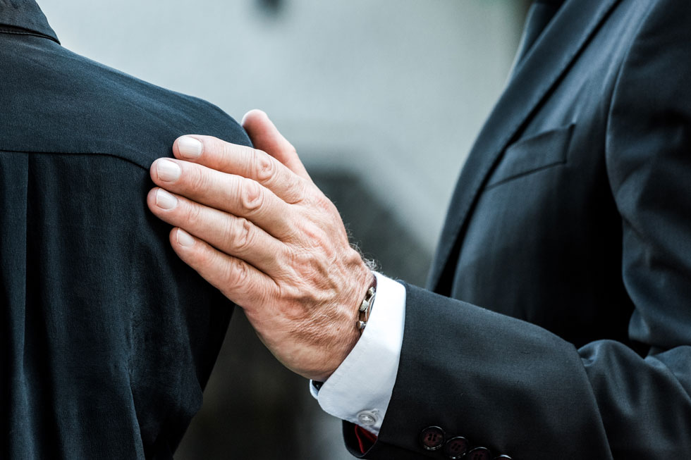 älterer Mann hält stützend Schulter einer trauernden Person